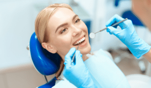 Woman receiving dental examination from dentist wearing blue gloves in clinical setting.