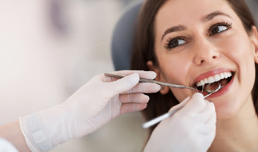 Smiling woman receiving dental examination from dentist in clinical setting with gloved hands.